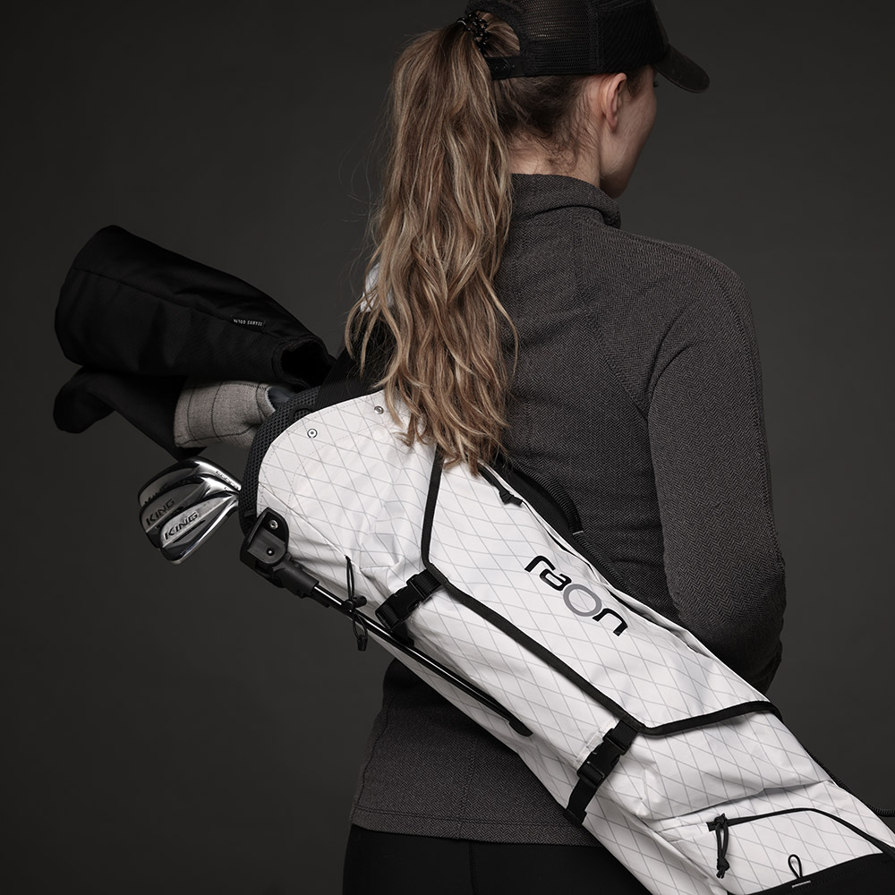 A young athletic woman has the whiteSunday Sling golf bag comfortably resting across her back